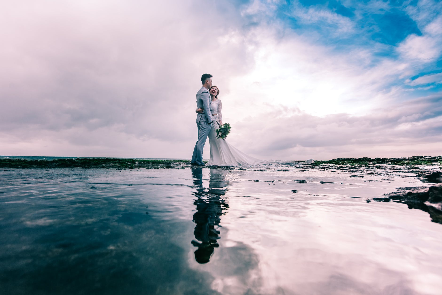 man in gray dress suit jacket embraces woman wearing wedding gown
